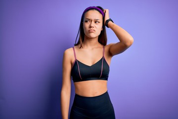 Obraz premium Young beautiful sporty girl doing sport wearing sportswear over isolated purple background confuse and wondering about question. Uncertain with doubt, thinking with hand on head. Pensive concept.