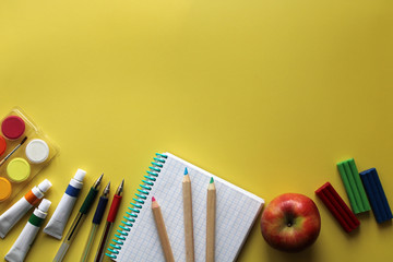 Top view of school stationery: paints, colored pencils, pen, plasticine and muffin on a background of colored paper. Back to school flat lay with copy space