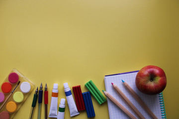 Top view of school stationery: paints, colored pencils, pen, plasticine and muffin on a background of colored paper. Back to school flat lay with copy space