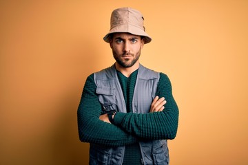 Handsome tourist man with beard on vacation wearing explorer hat over yellow background skeptic and...