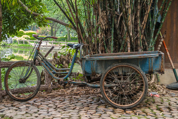 Fototapeta na wymiar Guilin, China - May 11, 2010: Seven Star Park. Closeup of blue transport tricycle with pedals in front of green and brown garden scenery.