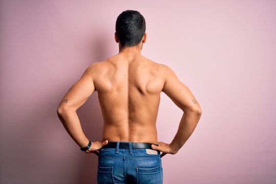 Young handsome strong man with beard shirtless standing over isolated pink background standing backwards looking away with arms on body