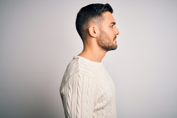 Young handsome man wearing casual sweater standing over isolated white background looking to side, relax profile pose with natural face with confident smile.