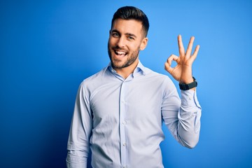 Young handsome man wearing elegant shirt standing over isolated blue background smiling positive...