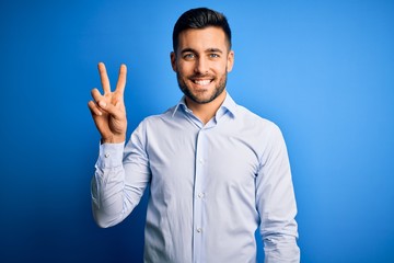 Young handsome man wearing elegant shirt standing over isolated blue background showing and pointing up with fingers number two while smiling confident and happy.