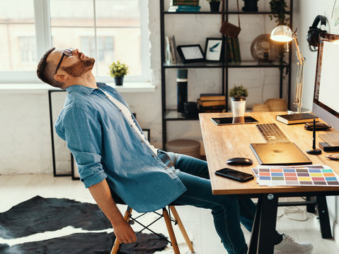 Exhausted man sitting at table with gadgets.