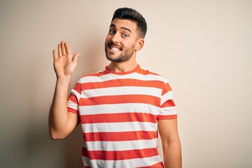 Young handsome man wearing casual striped t-shirt standing over isolated white background Waiving saying hello happy and smiling, friendly welcome gesture