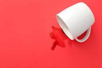 Overturned cup of coffee on color background