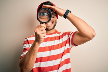 Young detective man looking through magnifying glass over isolated background stressed with hand on head, shocked with shame and surprise face, angry and frustrated. Fear and upset for mistake.