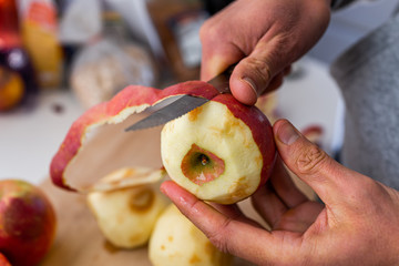 Macro closeup of wooden chopping cutting board and person hands peeling old red apples fruit after harvest for cooking ingredient