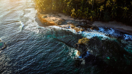 Aerial view of a tropical island near the ocean scenery surrounded by palm trees on a beach with white sand. View from the side