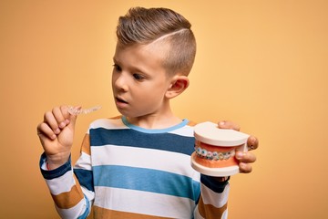 Little kid boy holding professional orthodontic denture with metal braces and removable invisible...