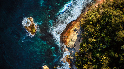 Aerial drone photo of a tiny island in a turquoise transparent water of an ocean, surrounded by sandy beach and palm trees of a tropical resort. View from the top