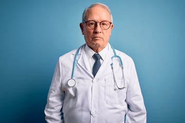 Senior grey haired doctor man wearing stethoscope and medical coat over blue background depressed...