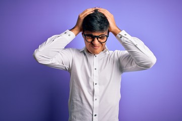 Young handsome business man wearing shirt and glasses over isolated purple background suffering from headache desperate and stressed because pain and migraine. Hands on head.