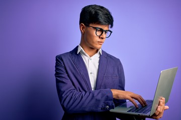 Young handsome business man wearing glasses working using laptop over purple background with a confident expression on smart face thinking serious