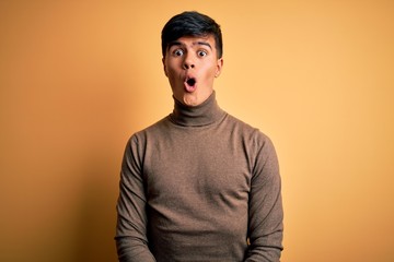 Fototapeta premium Young handsome man wearing casual turtleneck sweater over isolated yellow background afraid and shocked with surprise expression, fear and excited face.
