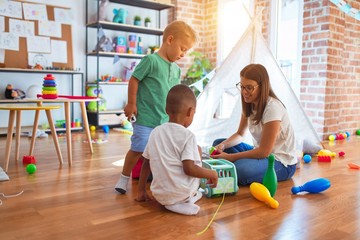 Young beautiful teacher and toddlers playing around lots of toys at kindergarten