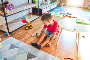 Adorable toddler playing with cars around lots of toys at kindergarten