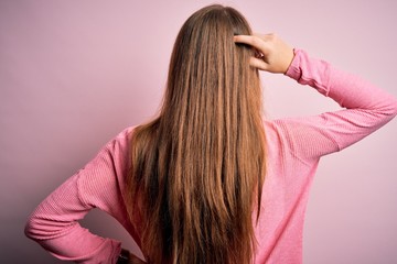 Young beautiful redhead woman wearing casual sweater over isolated pink background Backwards thinking about doubt with hand on head