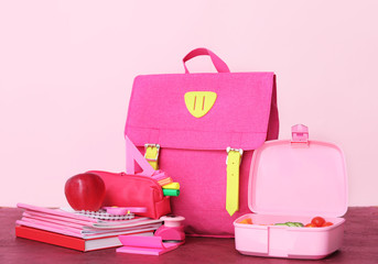 School backpack with lunch box and stationery on color background