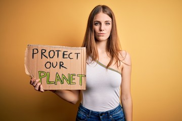 Young redhead woman asking for enviroment holding banner with protect planet message with a...