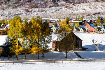 Aspen, Colorado rocky mountains with log wooden cabin at ranch farm pasture covered in snow after winter with yellow autumn trees and cityscape