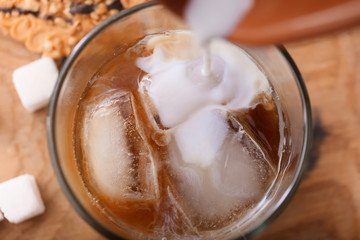 Pouring of milk into cold coffee in glass, closeup