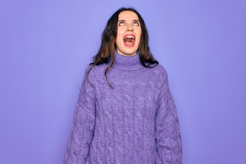 Fototapeta premium Young beautiful woman wearing casual turtleneck sweater standing over purple background angry and mad screaming frustrated and furious, shouting with anger. Rage and aggressive concept.