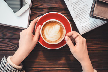Woman drinking tasty cappuccino at wooden table