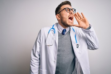 Young doctor man with blue eyes wearing medical coat and stethoscope over isolated background shouting and screaming loud to side with hand on mouth. Communication concept.