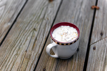 Closeup of one hot chocolate or coffee cup with festive marshmallow white foam cappuccino or Christmas cocoa drink on wooden table outside