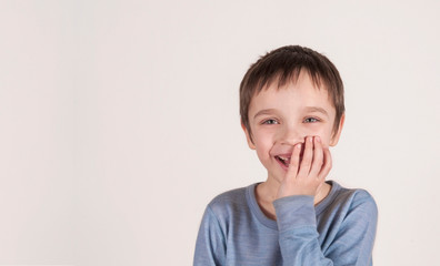 Happy adorable young boy smiling, covering his mouth with his hand. (concept human behavior)