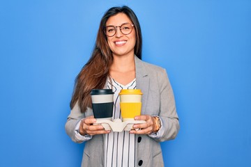 Young hispanic intern business woman holding coffee over blue background with a happy face standing...