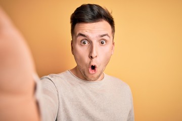 Young handsome caucasian man talking a selfie picture over yellow isolated background scared in shock with a surprise face, afraid and excited with fear expression