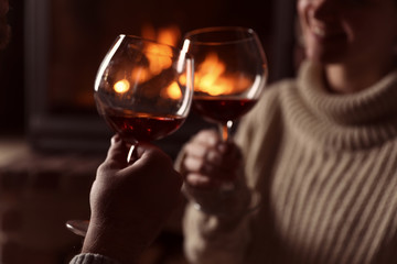 Lovely couple with glasses of wine near fireplace at home, closeup. Winter vacation