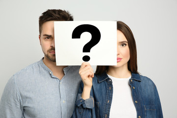 Couple holding question mark sign on light background