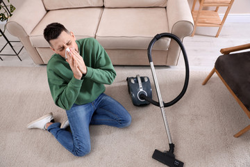 Man with vacuum cleaner suffering from dust allergy at home, above view