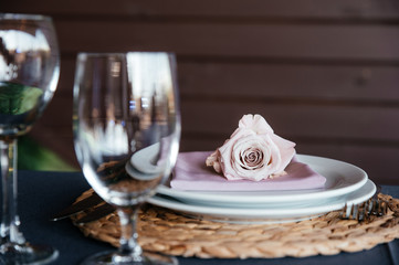 Romantic dinner. .Close-up photo of glass for wine and white round plate decorated with pastel pink bud of rose and pastel-pink napkins. Side view