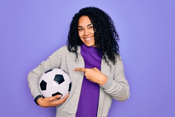 African american curly player woman playing soccer holding football bal over purple background very happy pointing with hand and finger