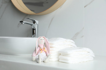 Stacks of baby diapers and toy bunny on counter in bathroom