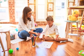 Beautiful teacher and toddler drawing using pencils and paper around lots of toys at kindergarten