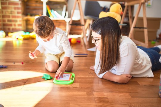 Beautiful teacher and toddler drawing using digital board around lots of toys at kindergarten