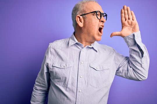 Middle age handsome hoary man wearing striped shirt and glasses over purple background shouting and screaming loud to side with hand on mouth. Communication concept.
