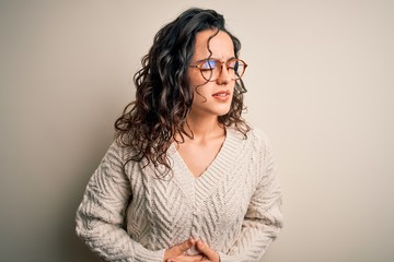 Beautiful woman with curly hair wearing casual sweater and glasses over white background with hand on stomach because nausea, painful disease feeling unwell. Ache concept.