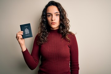 Young beautiful tourist woman with curly hair on vacation holding canadian canada passport with a confident expression on smart face thinking serious