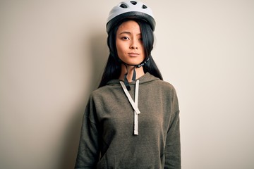 Young beautiful chinese woman wearing bike helmet over isolated white background Relaxed with serious expression on face. Simple and natural looking at the camera.