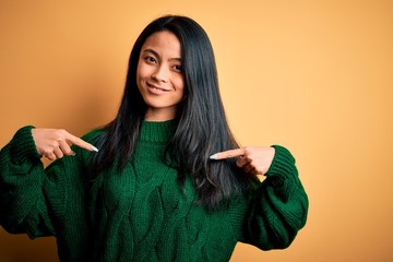 Young beautiful chinese woman wearing green sweater over isolated yellow background looking...