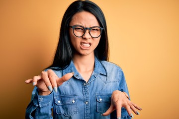 Young beautiful chinese woman wearing casual denim shirt over isolated yellow background smiling...