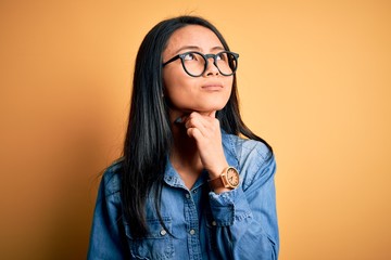 Young beautiful chinese woman wearing casual denim shirt over isolated yellow background Touching painful neck, sore throat for flu, clod and infection